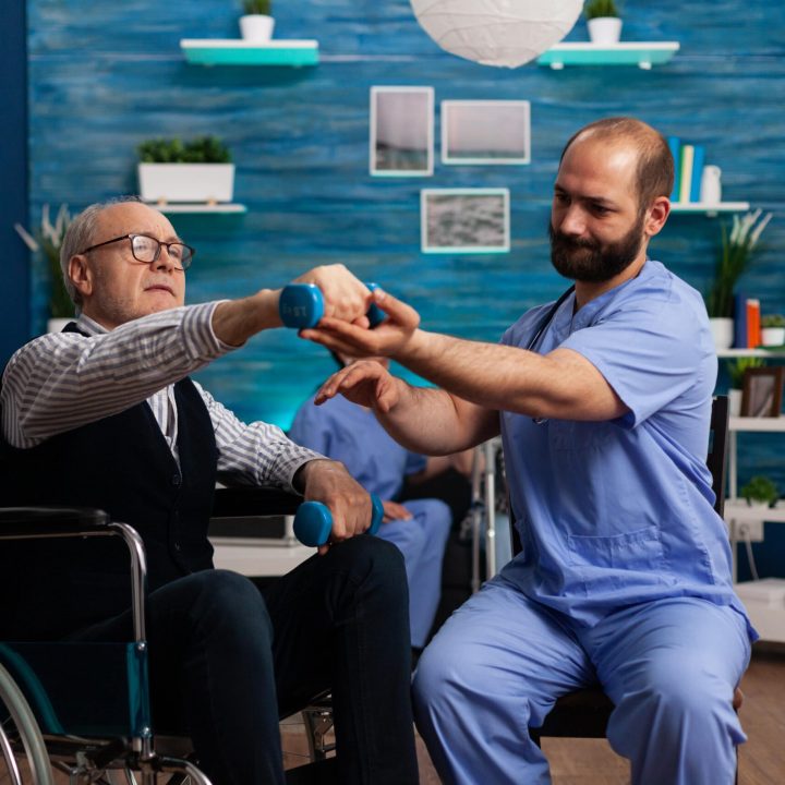practitioner-man-doctor-helping-retiree-senior-male-wheelchair-physiotherapy-strength-exercise-min